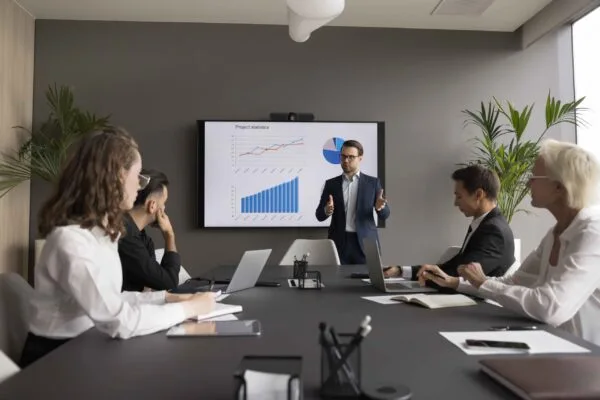 Businessman presents project statistics to diverse team in modern conference room.