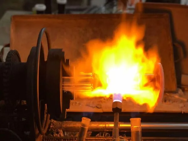 Industrial machine heating glass tubes with intense flame for manufacturing process.
