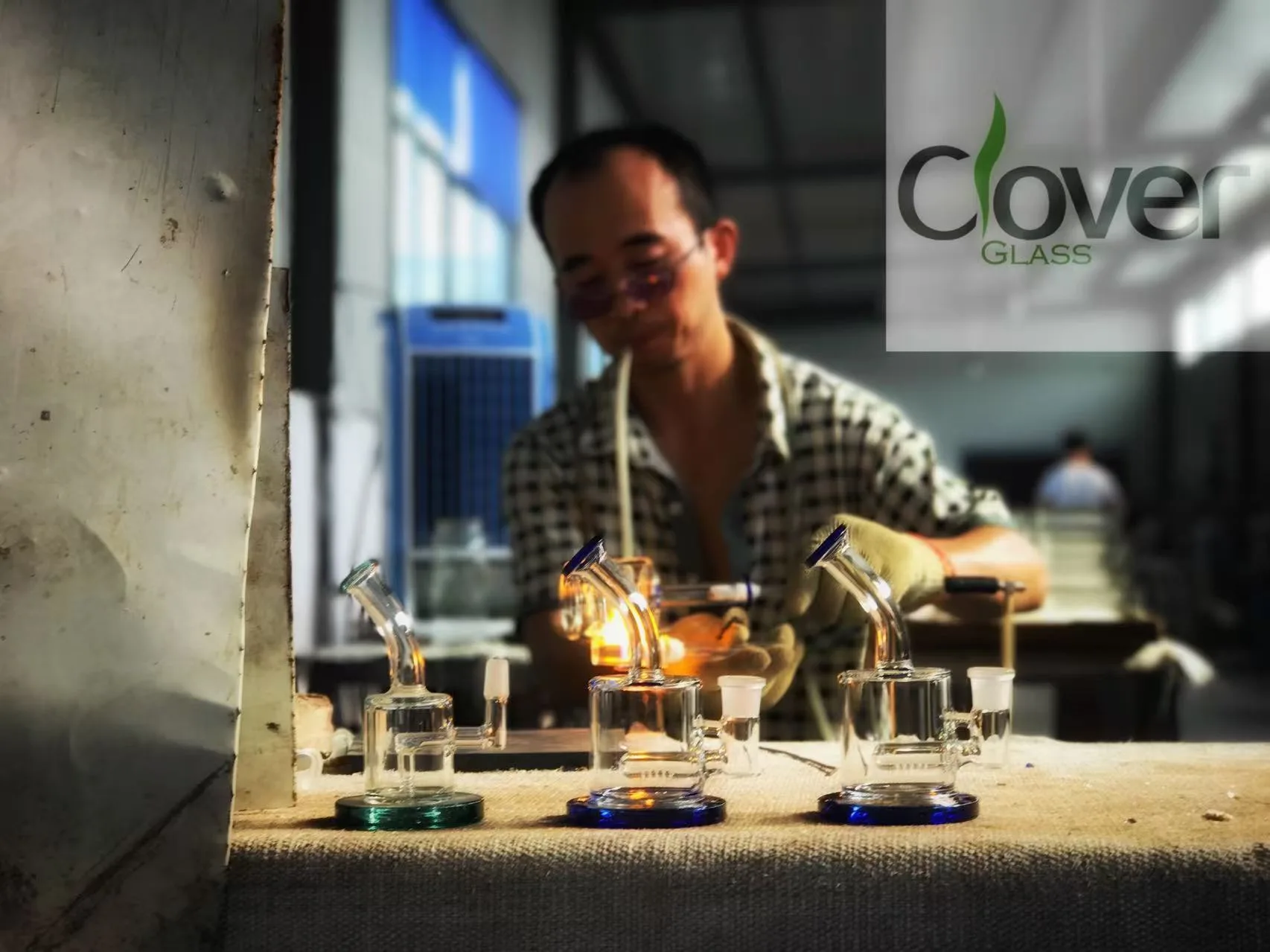 Artisan glassblower crafting Clover Glass water pipes with a torch in workshop.
