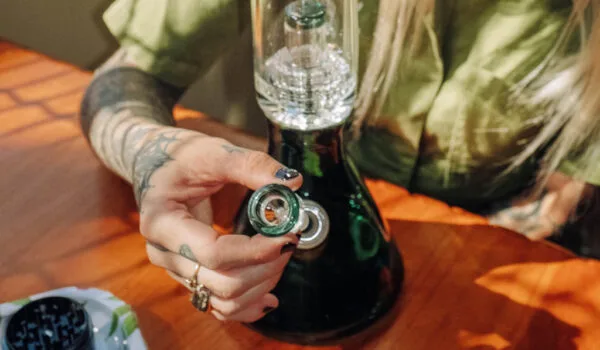 Tattooed hand holding a green glass bowl for a dark percolator bong.