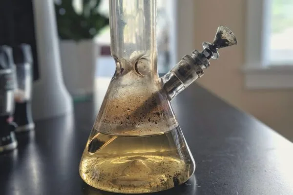 Dirty glass bong with murky water and dark resin buildup on a dark table.