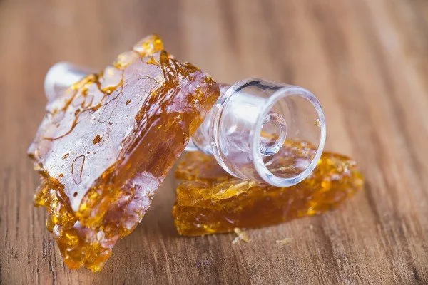 Amber cannabis shatter pieces and a clear glass dab banger on a wooden table.