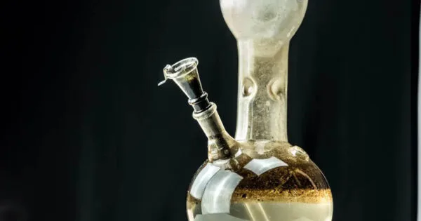 Used glass water pipe with dark liquid and brown residue on a black background.