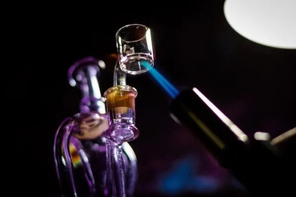 Glass dab rig with clear banger being heated by a blue torch flame.