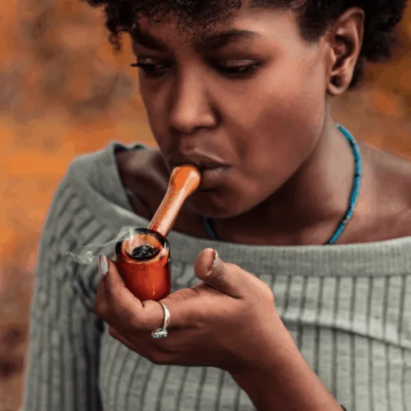Young woman smoking an orange pipe, smoke rising, wearing a ring.