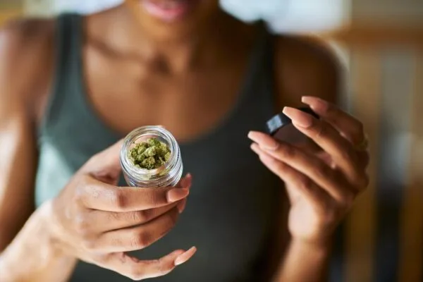 Woman's hands holding an open jar of green cannabis buds.