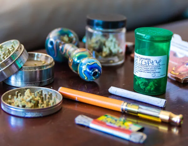 Colorful glass pipe, grinder, medical cannabis, vape pen, and pre-rolled joint on table.