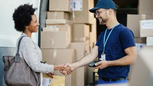 Smiling delivery driver and customer shaking hands, receiving a package.