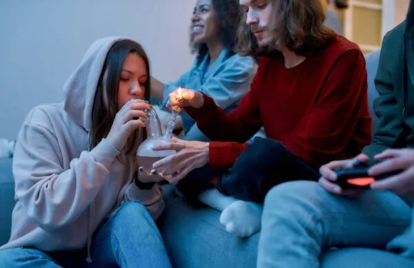 Young friends on couch smoking cannabis from a bong, playing video games.