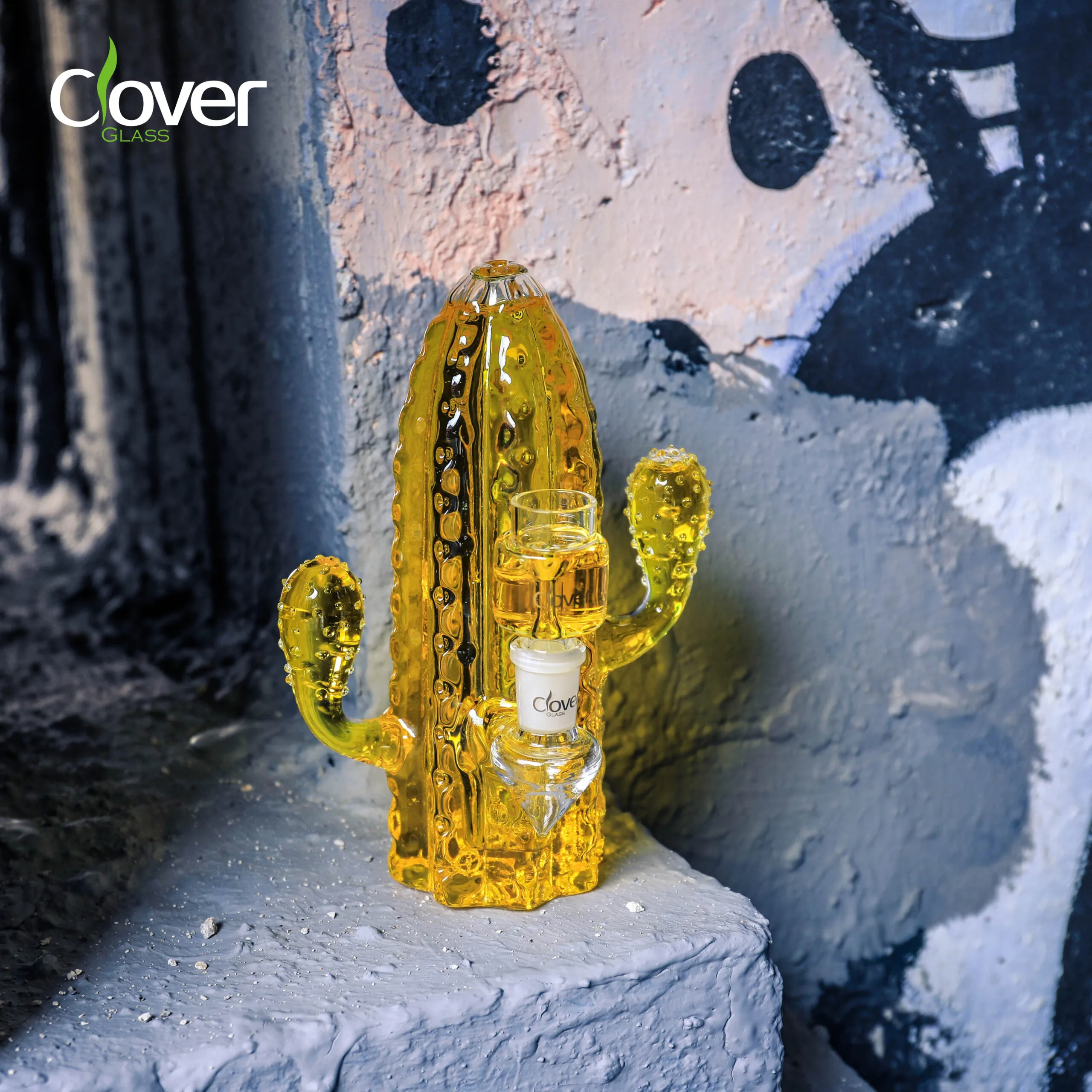 Vibrant yellow glass cactus bong by Clover Glass on a textured urban ledge.