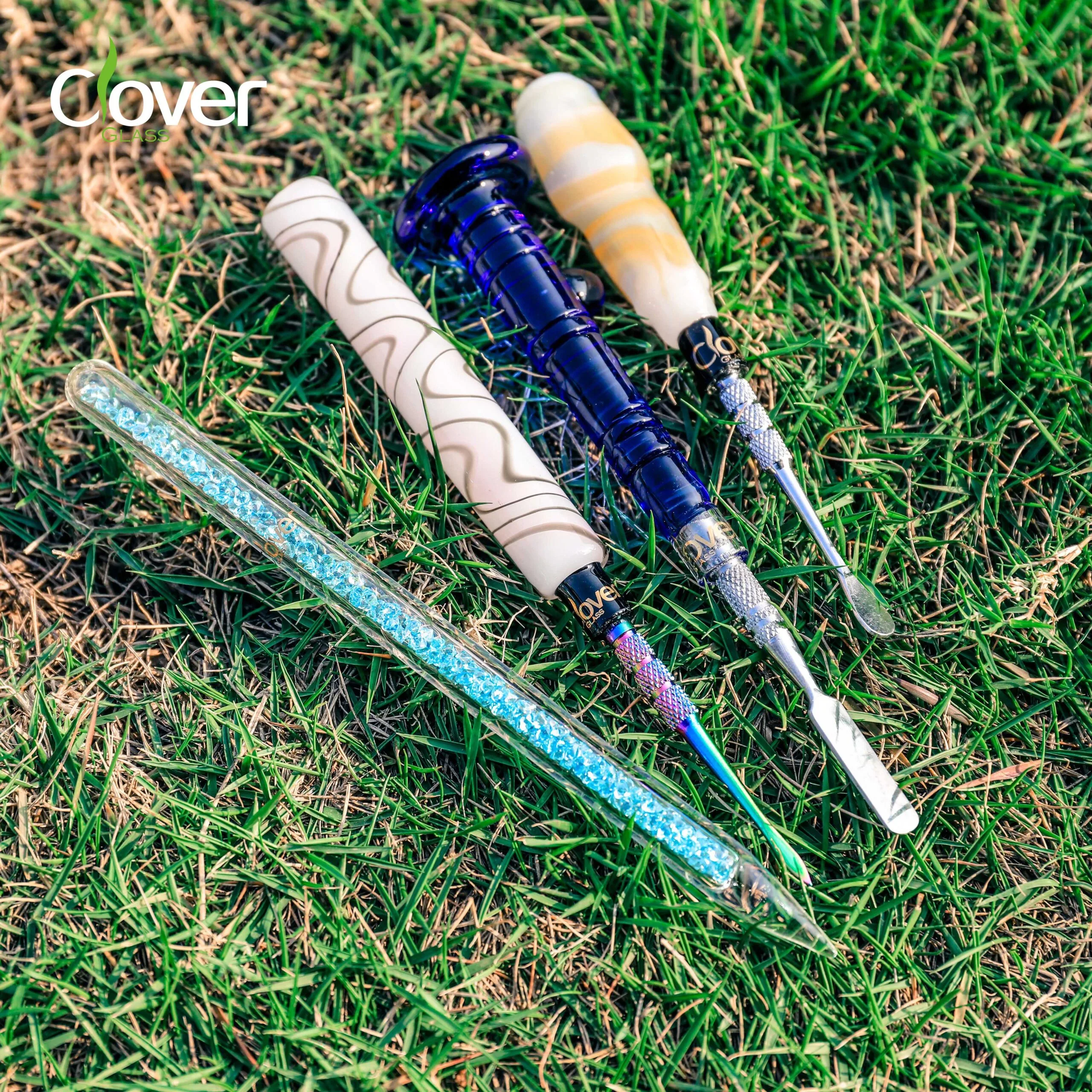 Four Clover Glass dab tools: crystal, blue, white, and orange designs on grass.
