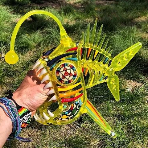 Vibrant yellow glass anglerfish art with colorful patterns, sharp teeth, held outdoors.