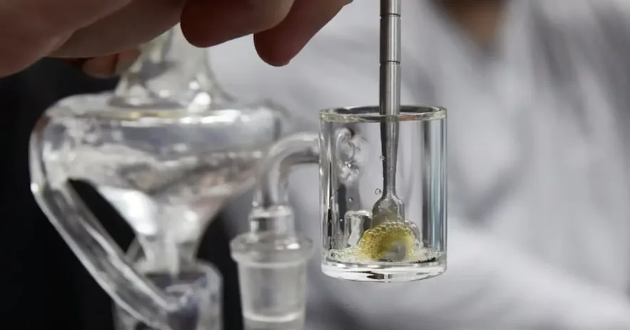 Close-up of a metal tool stirring yellow concentrate in a clear glass banger.