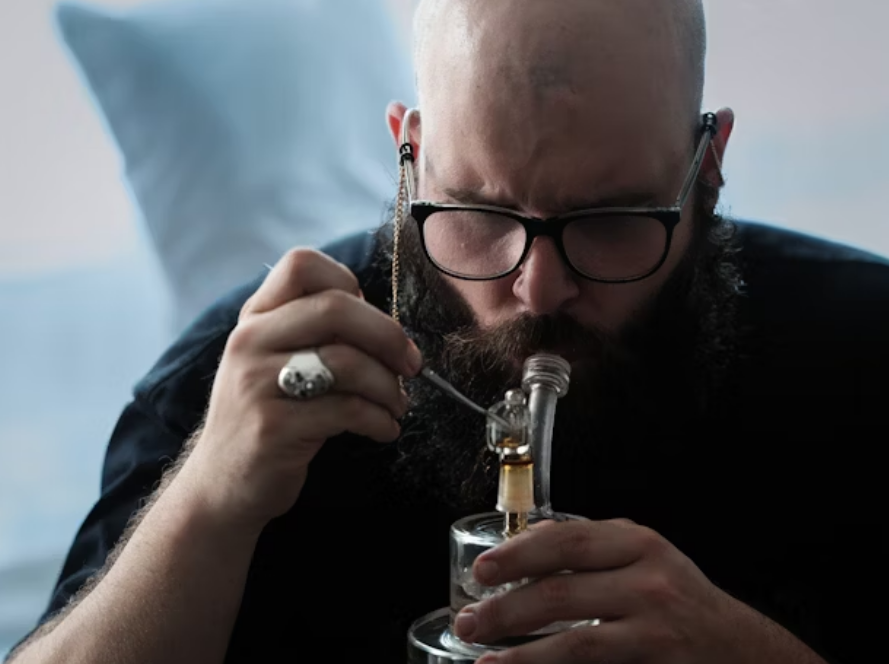 Bearded man using a glass dab rig with a quartz banger and dab tool indoors