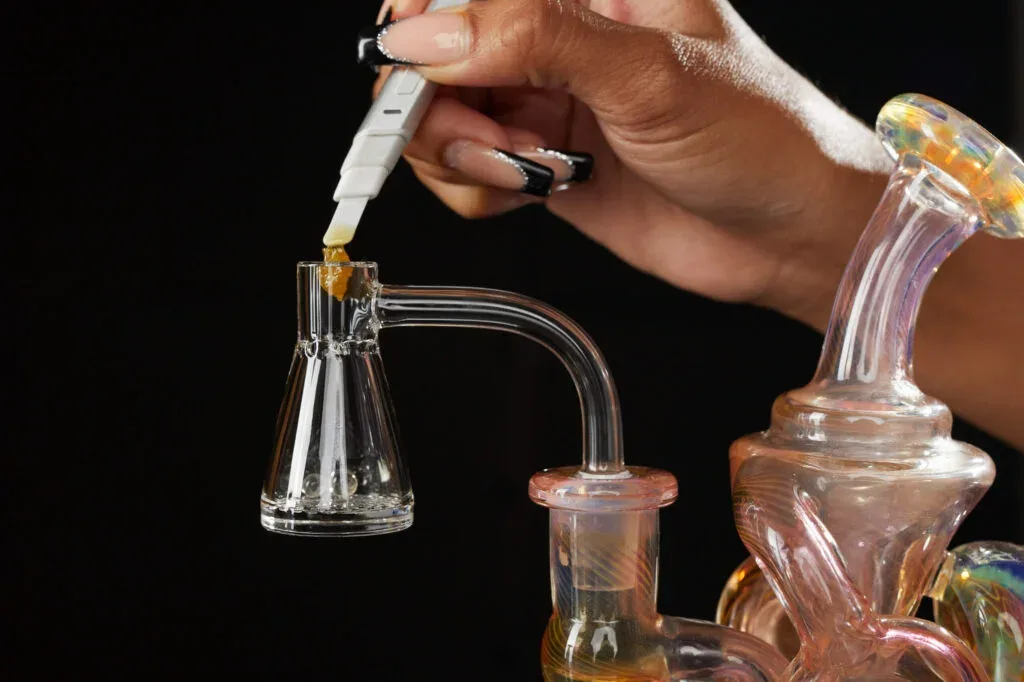 A person with manicured nails uses a dab tool to place cannabis concentrate into a quartz banger.