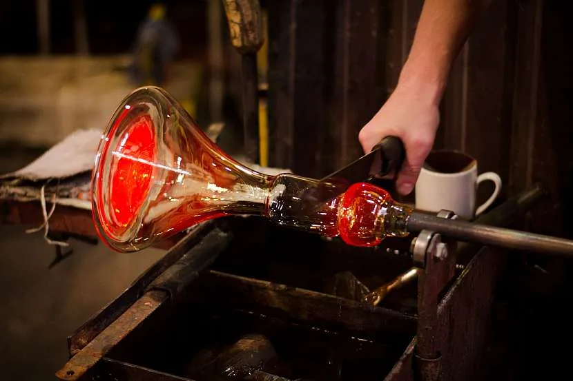Artisan's hand shaping glowing molten glass into a flared vessel during the glassblowing process.