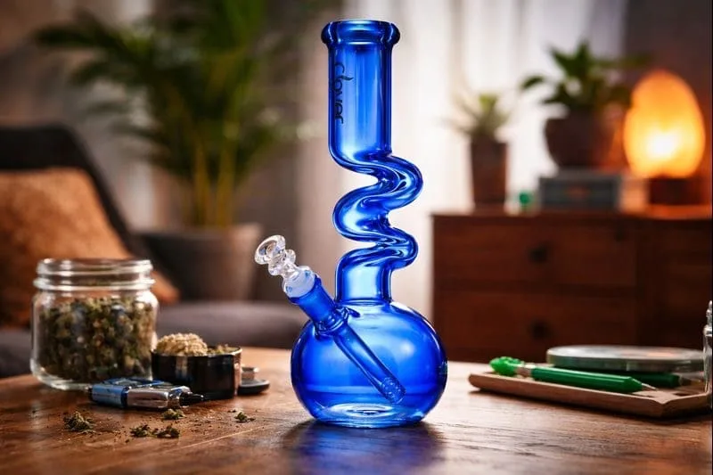 Vibrant blue Clover spiral glass bong with cannabis, grinder, and accessories on wood.