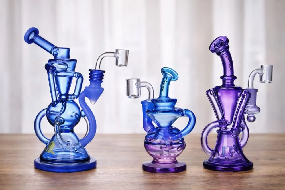 Three vibrant blue and purple glass dab rigs with unique designs and quartz bangers.