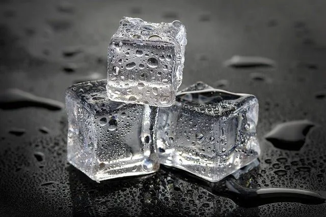 Three clear ice cubes with water droplets melting on a dark, reflective surface.