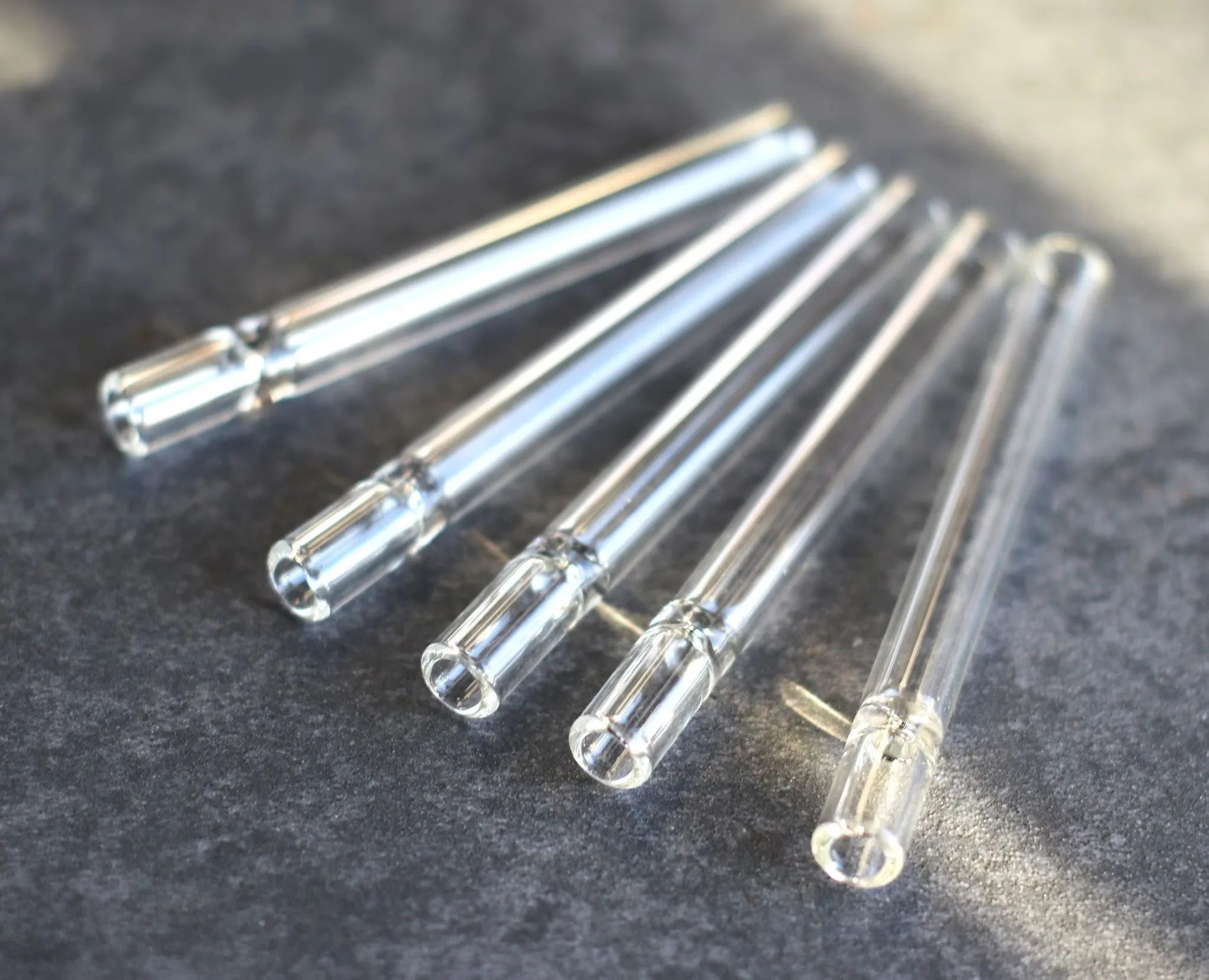 Five clear glass tubes with internal filters, lying on a dark textured surface.