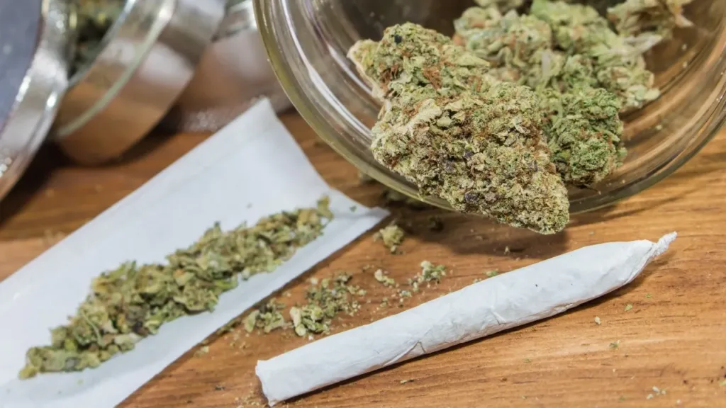 Cannabis buds in a glass bowl, loose weed on rolling paper, and a pre-rolled joint.
