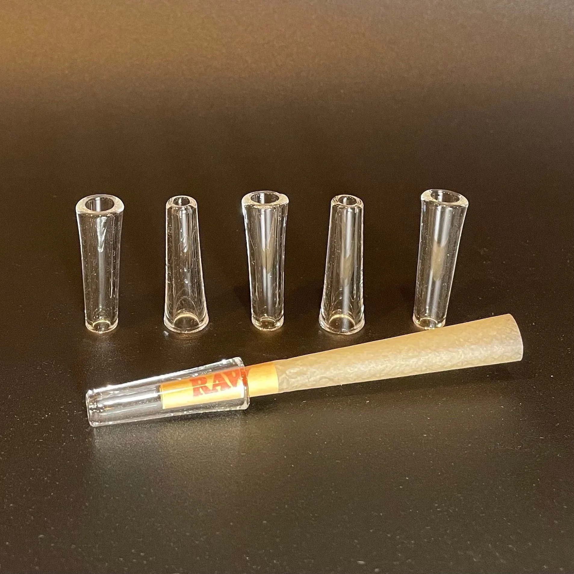 Five clear glass reusable filter tips with one attached to a RAW pre-roll.