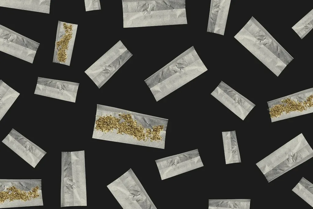 Scattered rolling papers, some with ground cannabis, on a dark background.