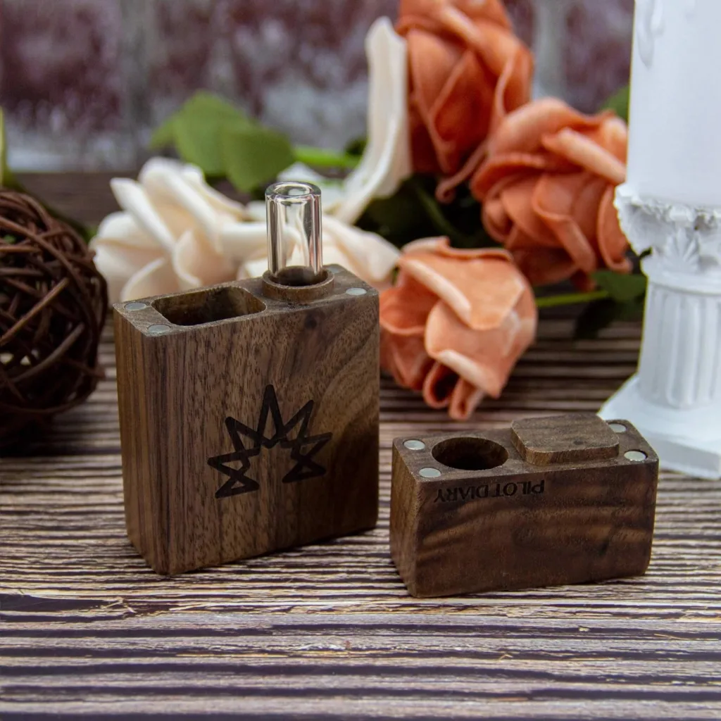 Two elegant dark wooden dry herb vaporizers with glass stem and engraved details on a rustic table.